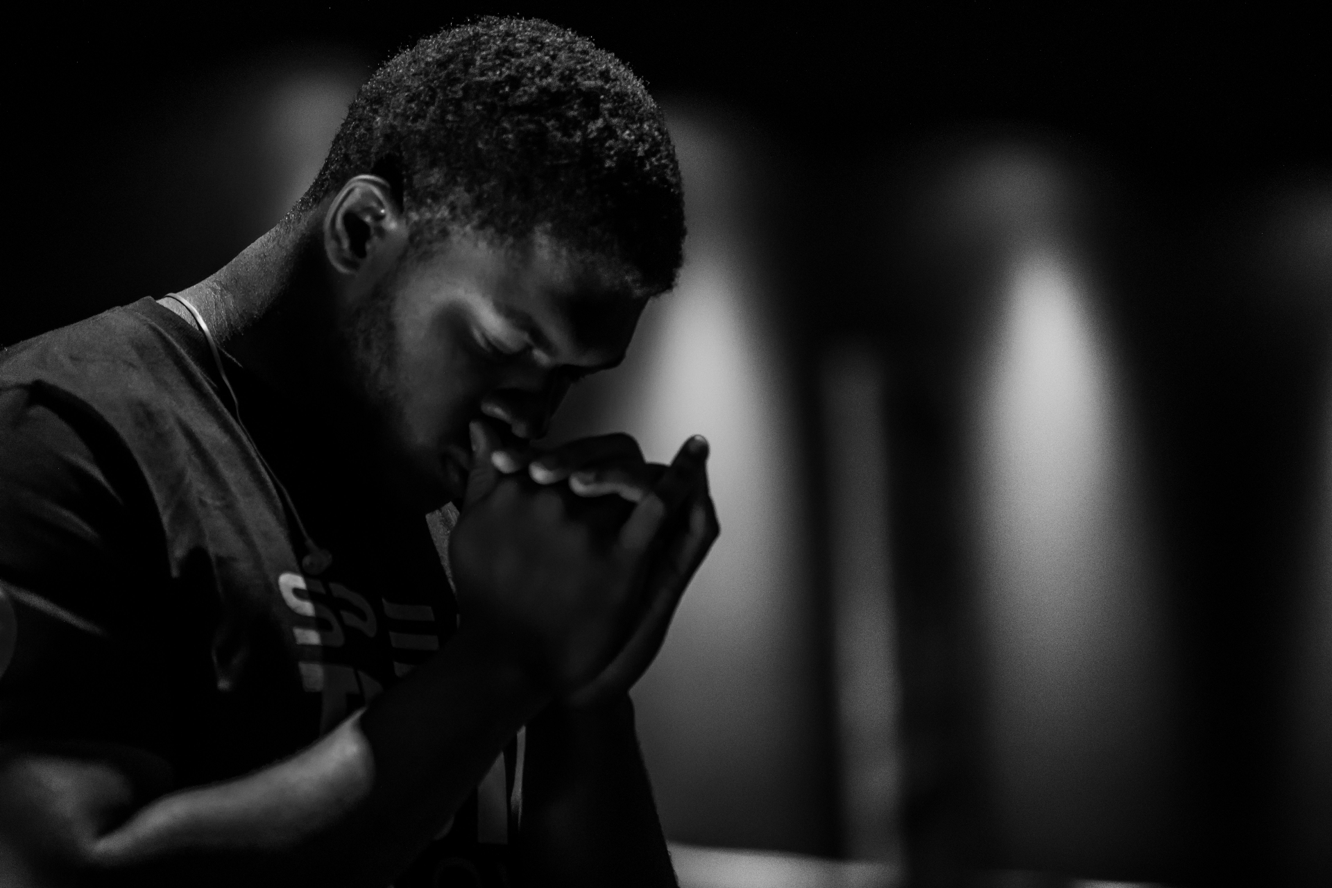 A man bowed in prayer, hands clasped near his face, in a quiet moment of intimate devotion